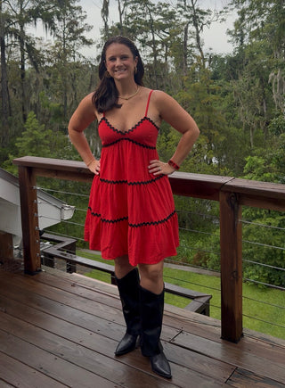Women stands on patio with red dress with wavy black details. 