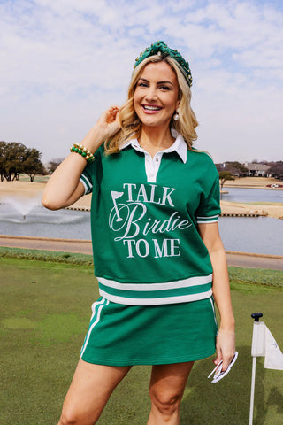 Woman in a green collared shirt with 'Talk Birdie To Me' text on a golf course