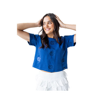 Woman wearing a blue slightly cropped top with embroidered UNC throughout shirt.