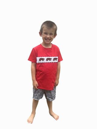 Child wearing a red shirt with smocked bear design and checkered shorts on a white background