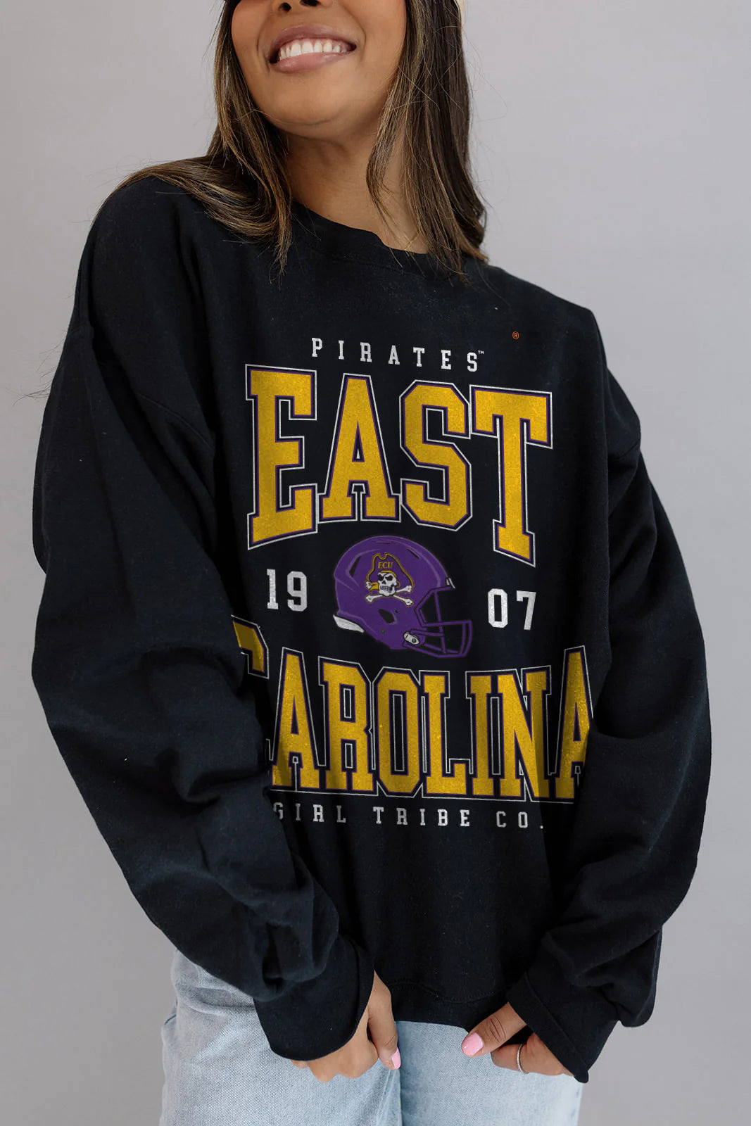 Person wearing a black 'East Carolina' sweatshirt with yellow text and a purple helmet graphic on a gray background.