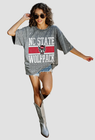 Person wearing a gray rhinestone 'NC State Wolfpack' t-shirt with denim shorts and cowboy boots on a white background