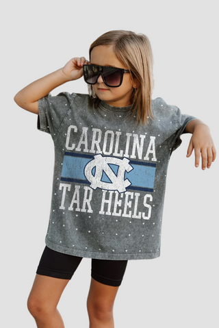Youth wearing a rhinestone Carolina Tar Heels shirt with sunglasses on a light gray background