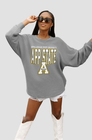 Woman wearing a gray sweatshirt with 'APP STATE' text, sunglasses, and white shorts in an outdoor setting.