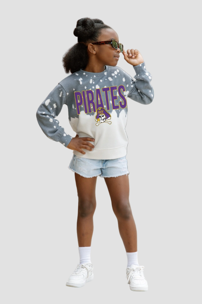 Girl wearing a 'Pirates' sweatshirt with a white shirt and denim shorts on a light gray background